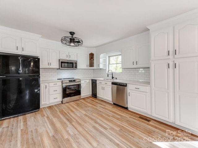 kitchen with appliances with stainless steel finishes, light hardwood / wood-style floors, sink, white cabinetry, and tasteful backsplash