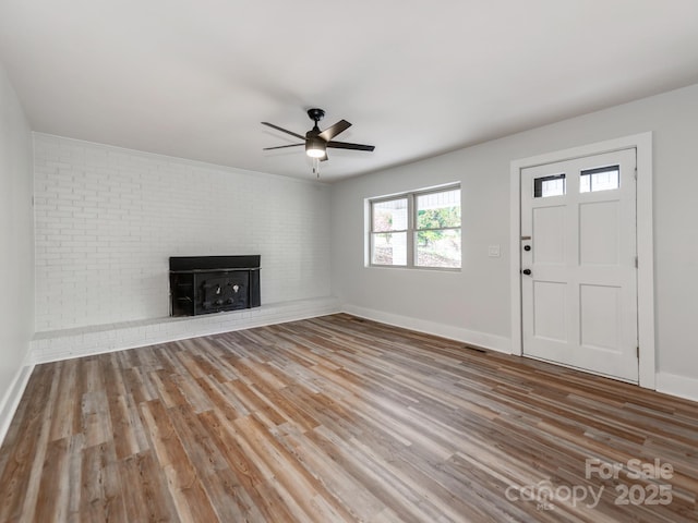 unfurnished living room featuring a brick fireplace, brick wall, ceiling fan, and light hardwood / wood-style floors