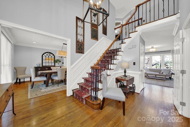 stairs featuring hardwood / wood-style flooring, a towering ceiling, crown molding, and an inviting chandelier