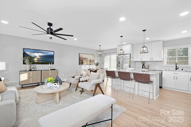 living room featuring ceiling fan, sink, and light wood-type flooring