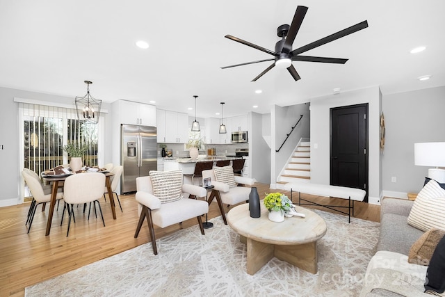 living room with ceiling fan with notable chandelier and light wood-type flooring