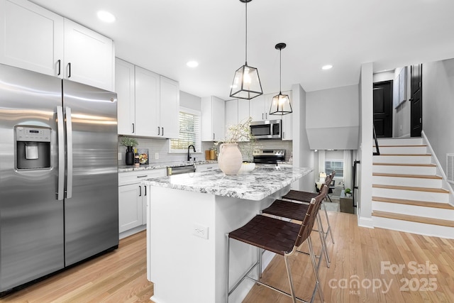 kitchen featuring tasteful backsplash, stainless steel appliances, a kitchen island, pendant lighting, and white cabinetry