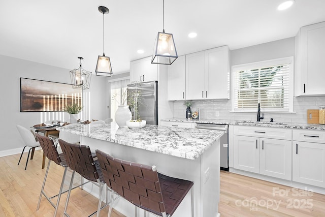 kitchen featuring a center island, hanging light fixtures, light stone countertops, white cabinetry, and stainless steel appliances