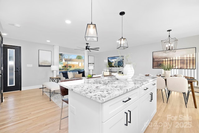 kitchen featuring white cabinets, pendant lighting, a center island, and light stone counters