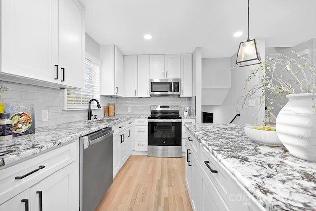 kitchen with pendant lighting, white cabinets, sink, appliances with stainless steel finishes, and light stone counters