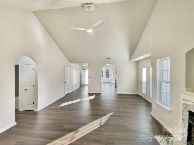 unfurnished living room with a high end fireplace, ceiling fan, dark wood-type flooring, and a high ceiling