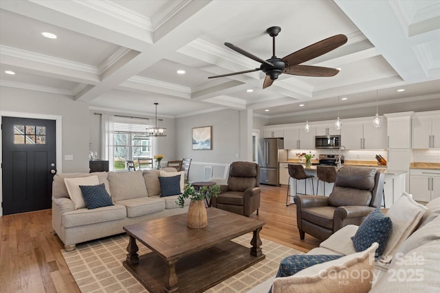 living room with beamed ceiling, ceiling fan with notable chandelier, coffered ceiling, and ornamental molding