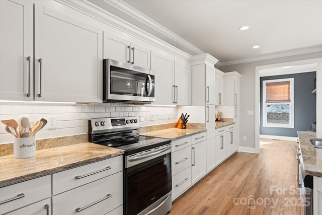 kitchen with light stone countertops, appliances with stainless steel finishes, white cabinetry, decorative backsplash, and ornamental molding