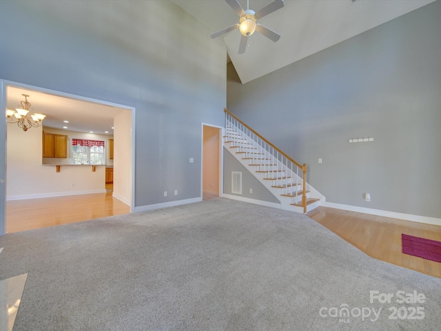 unfurnished living room featuring ceiling fan with notable chandelier, light colored carpet, and high vaulted ceiling