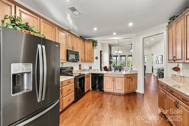 kitchen featuring visible vents, black appliances, a sink, wood finished floors, and light stone countertops