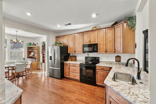 kitchen with sink, light hardwood / wood-style floors, hanging light fixtures, a chandelier, and black appliances