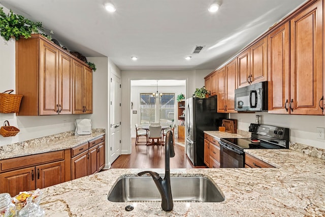 kitchen with black appliances, brown cabinetry, visible vents, and a sink