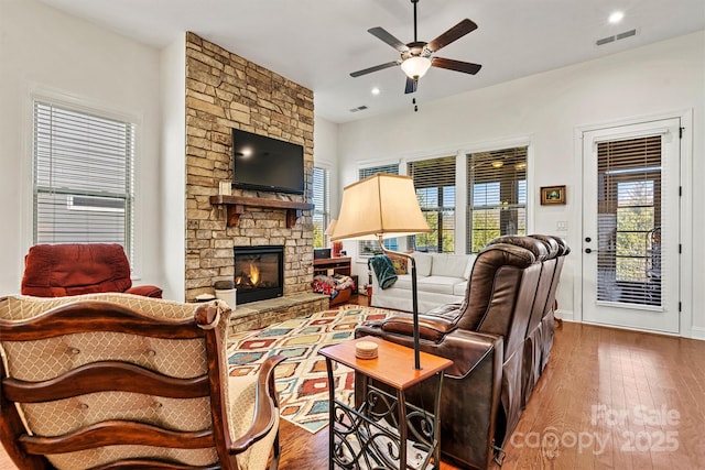 living area featuring visible vents, a stone fireplace, wood finished floors, and a ceiling fan