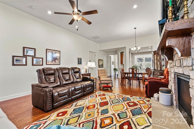 living room featuring ceiling fan with notable chandelier, a stone fireplace, and hardwood / wood-style floors