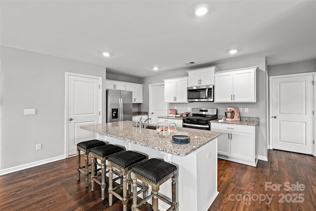 kitchen featuring a kitchen breakfast bar, light stone counters, stainless steel appliances, a center island with sink, and white cabinets