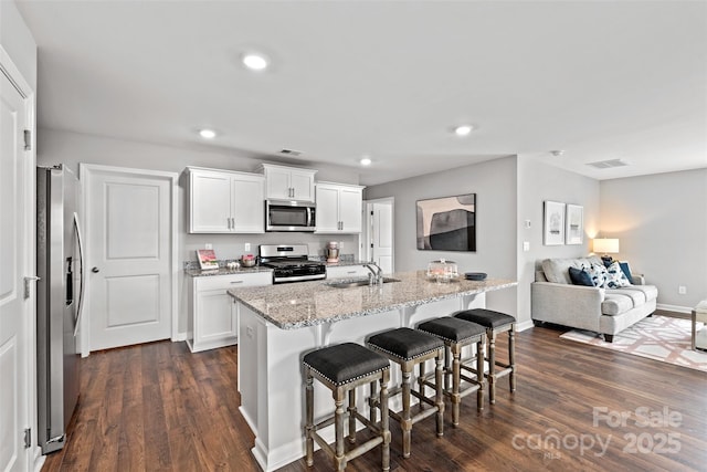 kitchen featuring a breakfast bar, white cabinets, a center island with sink, light stone counters, and stainless steel appliances