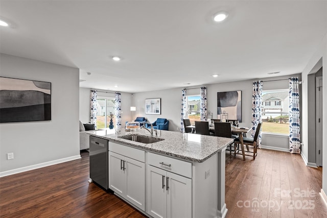 kitchen with white cabinets, light stone counters, sink, dishwasher, and an island with sink