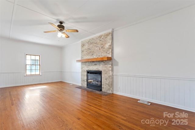 unfurnished living room with ceiling fan, wood-type flooring, ornamental molding, and a fireplace