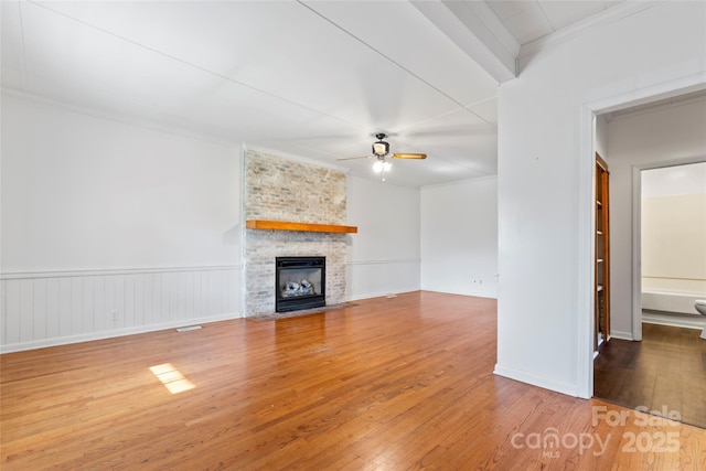 unfurnished living room featuring a fireplace, wood-type flooring, ceiling fan, and ornamental molding