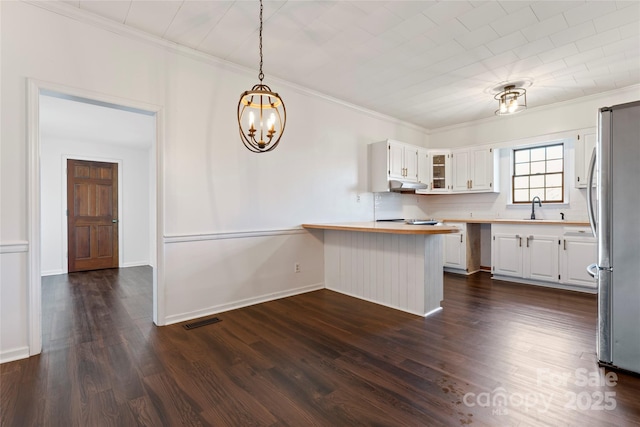 kitchen with kitchen peninsula, stainless steel fridge, backsplash, decorative light fixtures, and white cabinetry