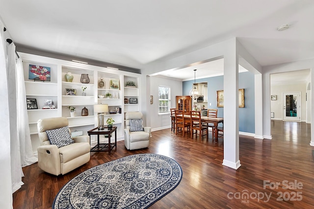 living area with built in features, dark hardwood / wood-style floors, and a notable chandelier