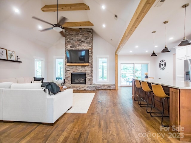 living room with beam ceiling, a stone fireplace, and high vaulted ceiling