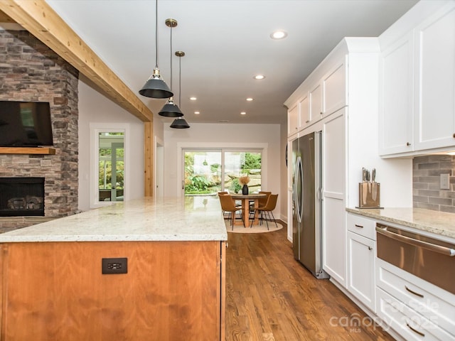 kitchen with pendant lighting, white cabinets, a fireplace, light stone counters, and stainless steel refrigerator