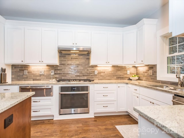 kitchen with backsplash, white cabinetry, stainless steel appliances, and light stone counters