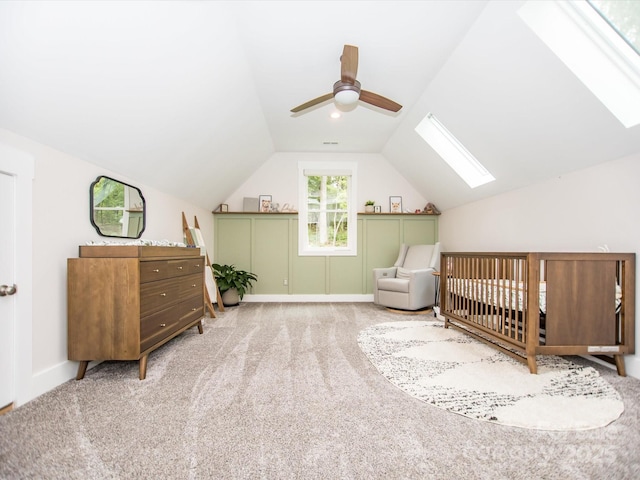 carpeted bedroom featuring ceiling fan, lofted ceiling with skylight, and a nursery area