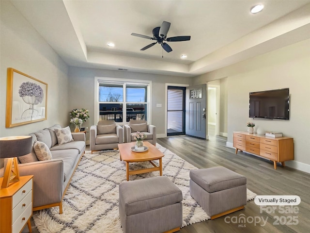 living room with hardwood / wood-style flooring, ceiling fan, and a raised ceiling