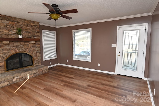 unfurnished living room with ornamental molding, a textured ceiling, ceiling fan, wood-type flooring, and a stone fireplace