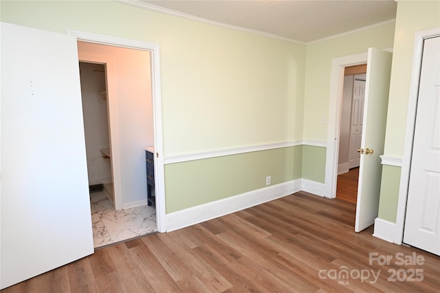 unfurnished bedroom featuring wood-type flooring, a spacious closet, a closet, and ornamental molding