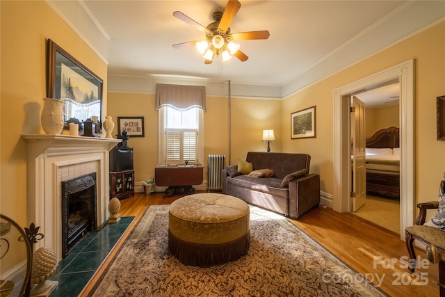 living room with wood-type flooring, crown molding, ceiling fan, a fireplace, and radiator heating unit