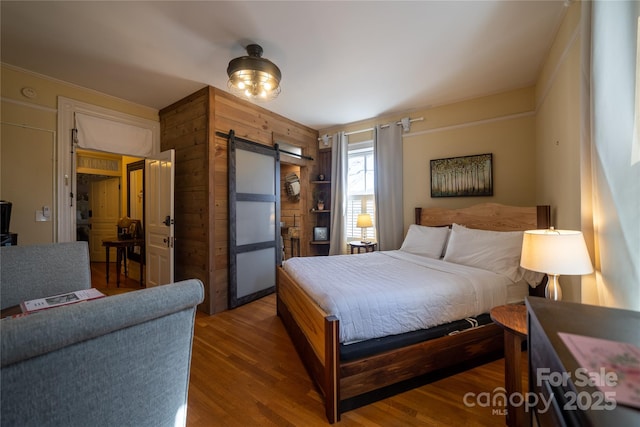 bedroom with a barn door, wooden walls, and wood-type flooring