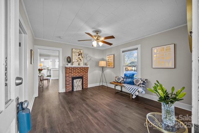 living area featuring dark wood-type flooring, ceiling fan, a brick fireplace, and crown molding