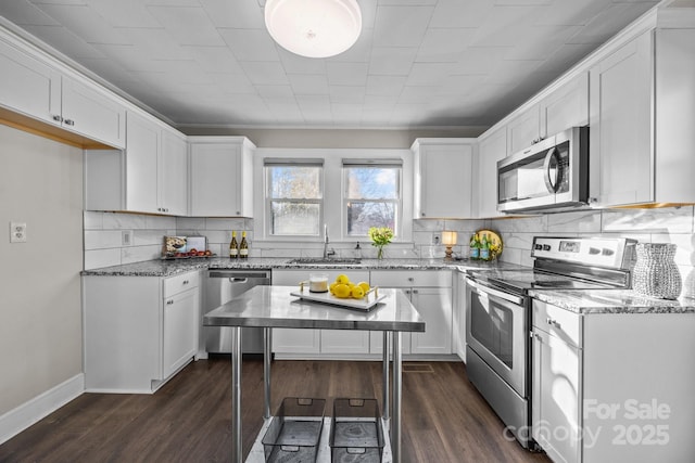 kitchen with white cabinetry, appliances with stainless steel finishes, dark hardwood / wood-style flooring, light stone countertops, and sink