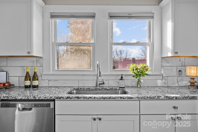 kitchen featuring tasteful backsplash, stainless steel dishwasher, sink, white cabinetry, and light stone countertops