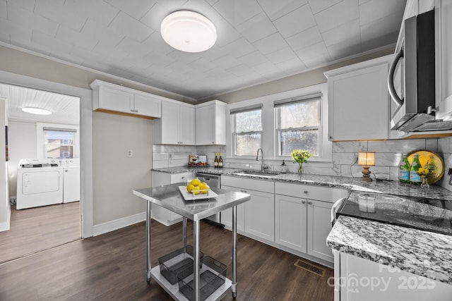 kitchen with sink, washing machine and clothes dryer, light stone countertops, appliances with stainless steel finishes, and white cabinets