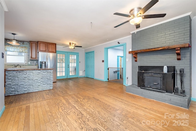 unfurnished living room featuring french doors, light wood-type flooring, ceiling fan, crown molding, and a fireplace