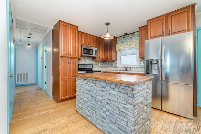 kitchen with a center island, sink, ornamental molding, decorative light fixtures, and stainless steel appliances