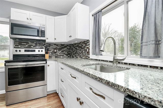 kitchen with light stone countertops, sink, stainless steel appliances, white cabinets, and light wood-type flooring