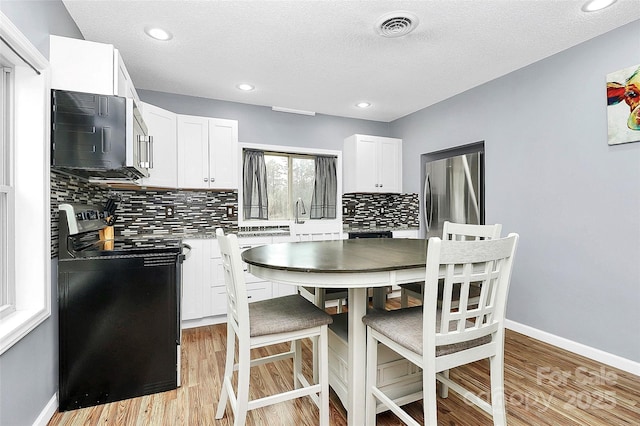 kitchen featuring a textured ceiling, electric range, white cabinets, light hardwood / wood-style floors, and stainless steel refrigerator