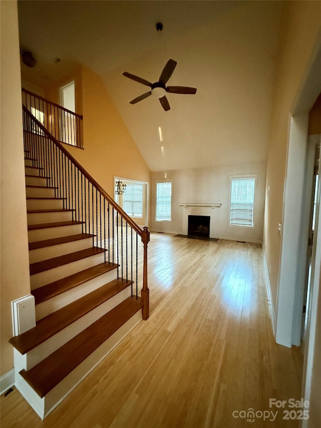 unfurnished living room featuring ceiling fan, plenty of natural light, high vaulted ceiling, and light wood-type flooring