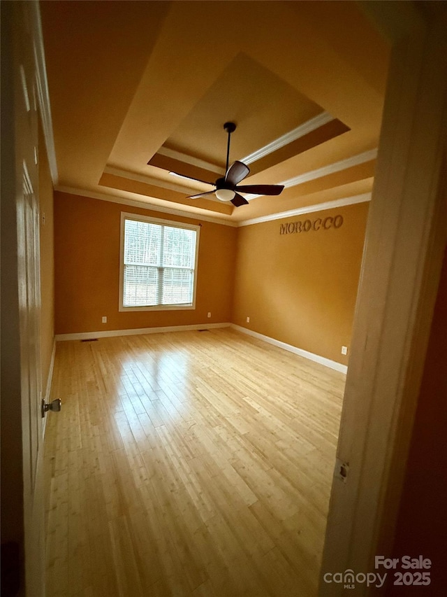 empty room with a tray ceiling, ceiling fan, light hardwood / wood-style floors, and ornamental molding