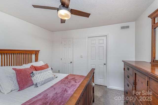 bedroom with a textured ceiling, dark carpet, visible vents, and a ceiling fan