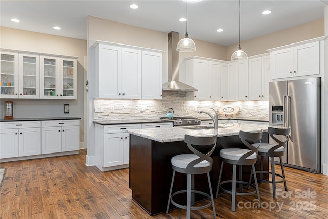 kitchen featuring dark wood-style floors, a breakfast bar, high end refrigerator, a sink, and wall chimney exhaust hood