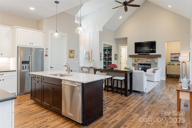 kitchen with a fireplace, appliances with stainless steel finishes, white cabinets, a sink, and wood finished floors