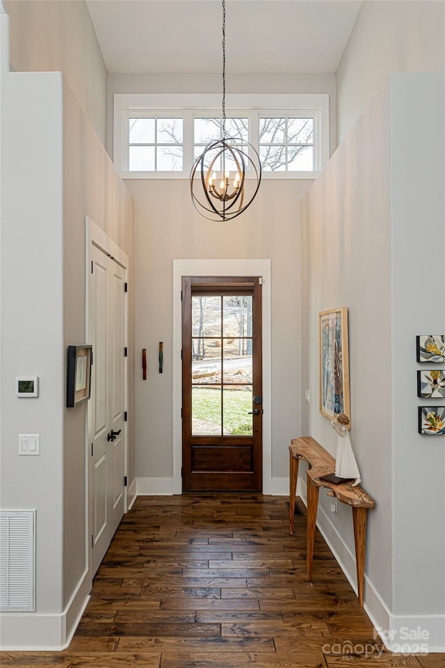 foyer entrance with dark hardwood / wood-style flooring, a notable chandelier, plenty of natural light, and a high ceiling