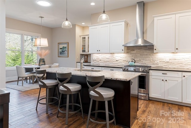 kitchen featuring sink, a kitchen island with sink, stainless steel gas range oven, white cabinets, and wall chimney exhaust hood