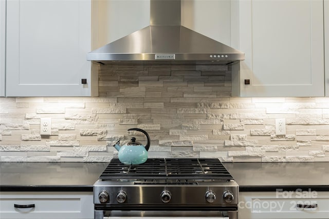 kitchen with stainless steel gas range oven, wall chimney range hood, white cabinets, and decorative backsplash